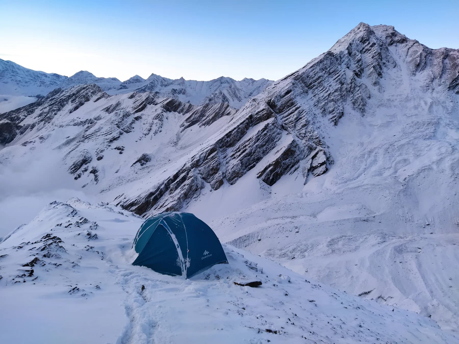 A single blue tent pitched on a snowy ridge beneath Himalayan mountains