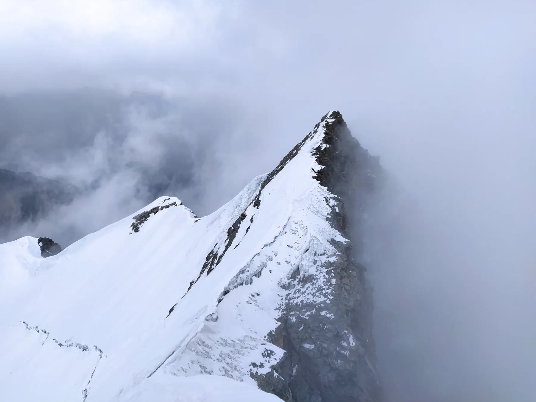 A narrow snow ridge and steep summit tower emerging through cloud
