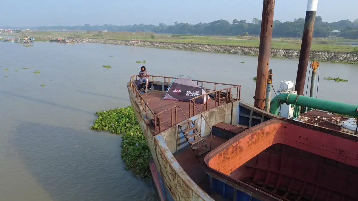 A small expedition tent on the open deck of a large vessel beside a riverbank