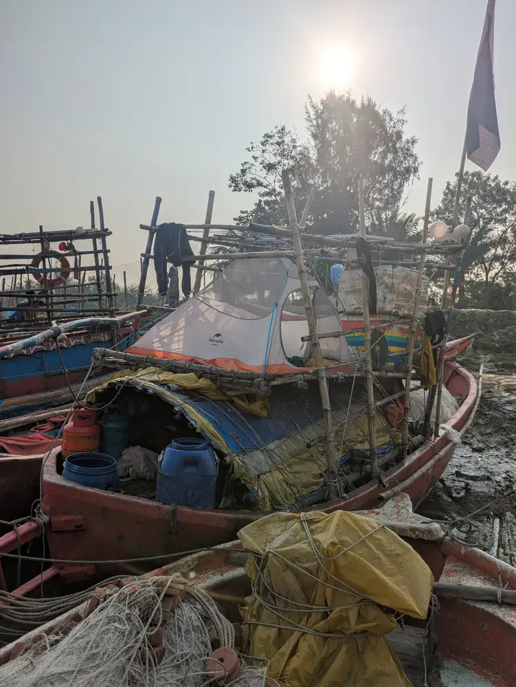 An expedition tent pitched among bamboo rails and gear on a fishing boat