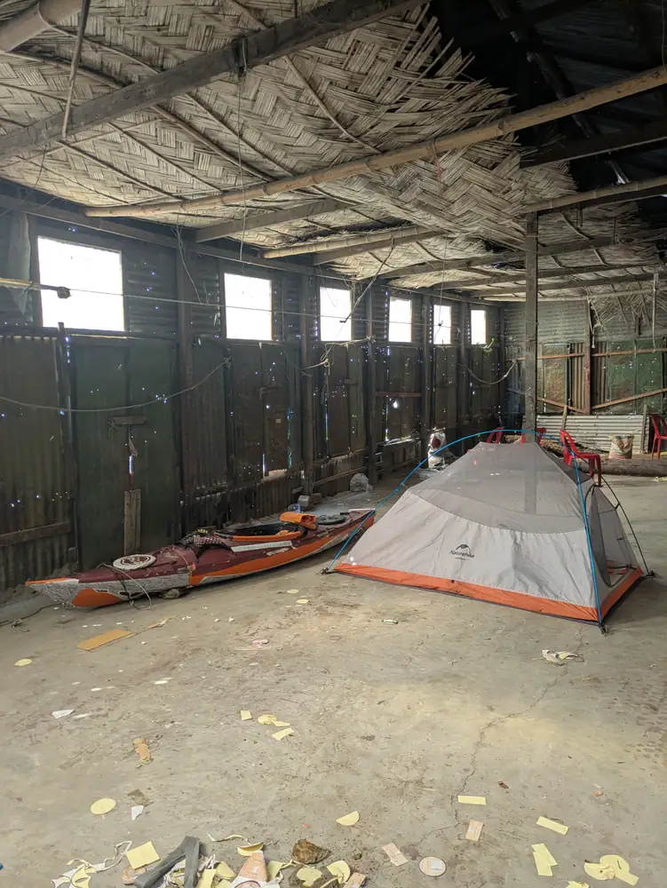 A tent and orange kayak inside a large shelter with woven bamboo roofing