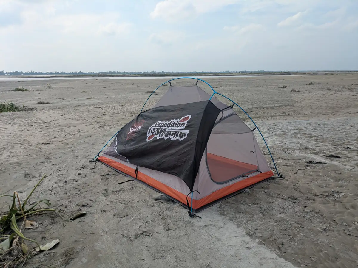 An expedition tent with the Teesta–Teknaf banner on an open sandy river char