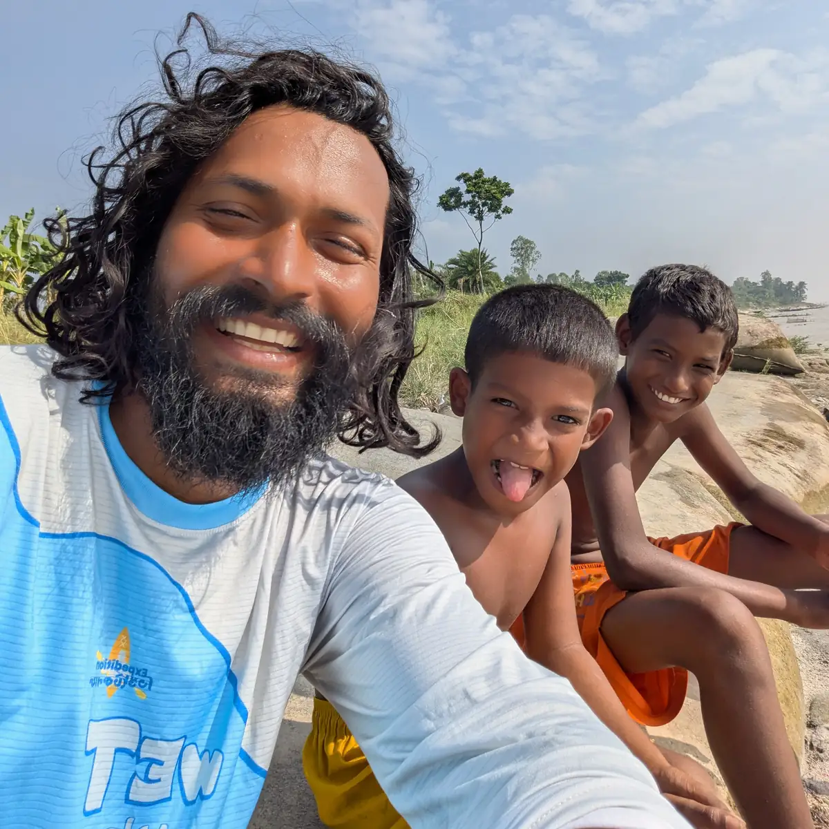 Intiaz Mahmud smiles for a selfie with two children beside the river