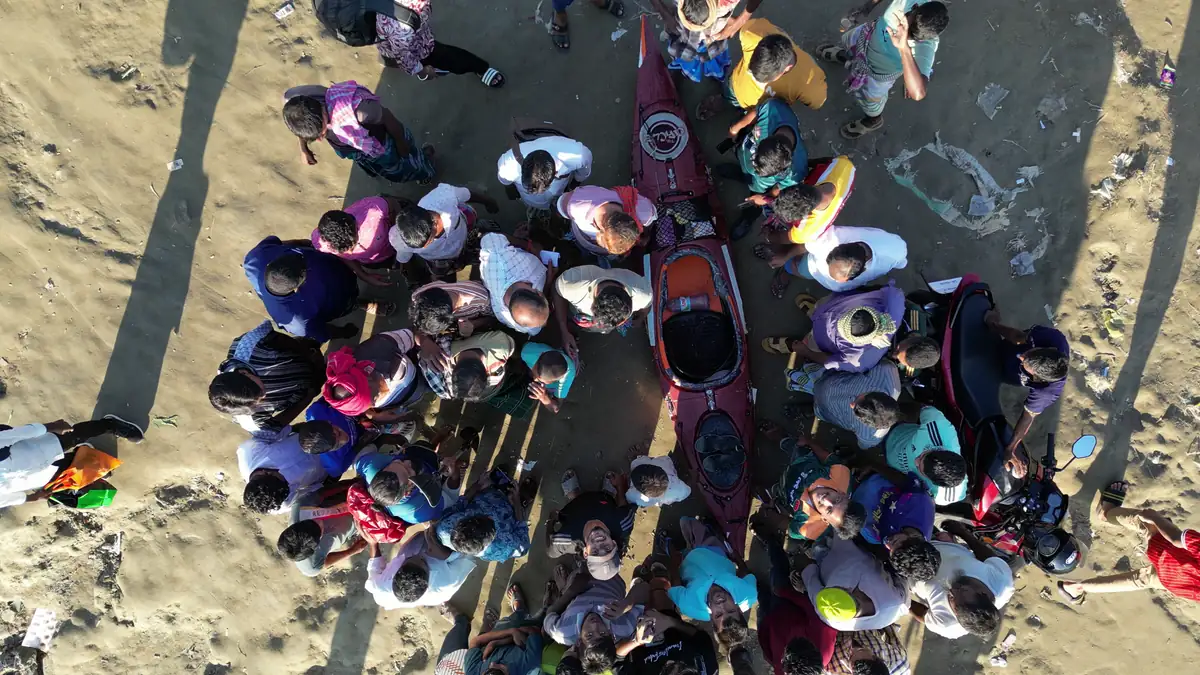 An overhead view of people gathered around the expedition kayak on a riverbank