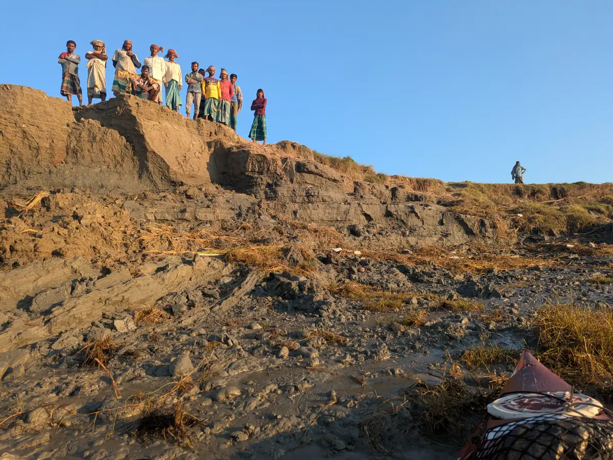 People look down from a high riverbank towards the kayak below