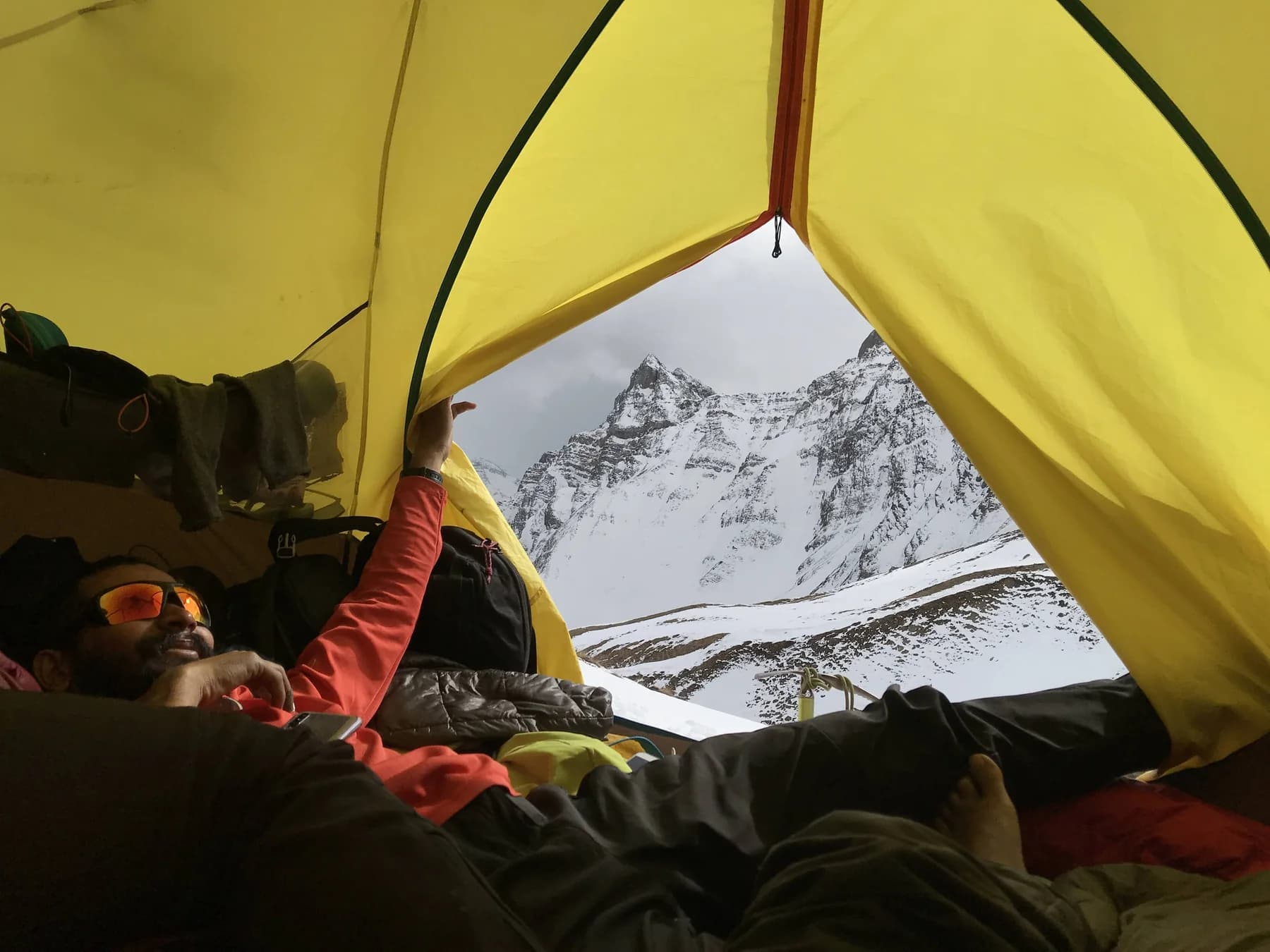 Intiaz resting inside a yellow tent, its open doorway framing snowy mountain peaks